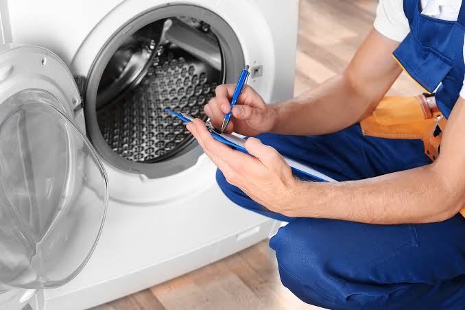 Technician recording observations while inspecting a front-loading washing machine
