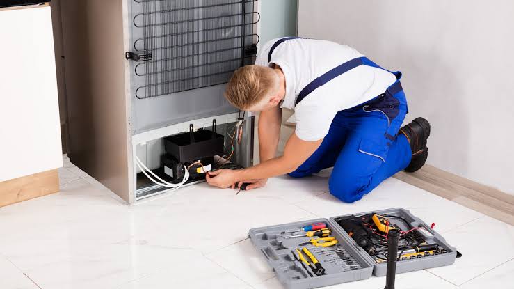 Technician inspecting the rear cooling components of a residential freezer
