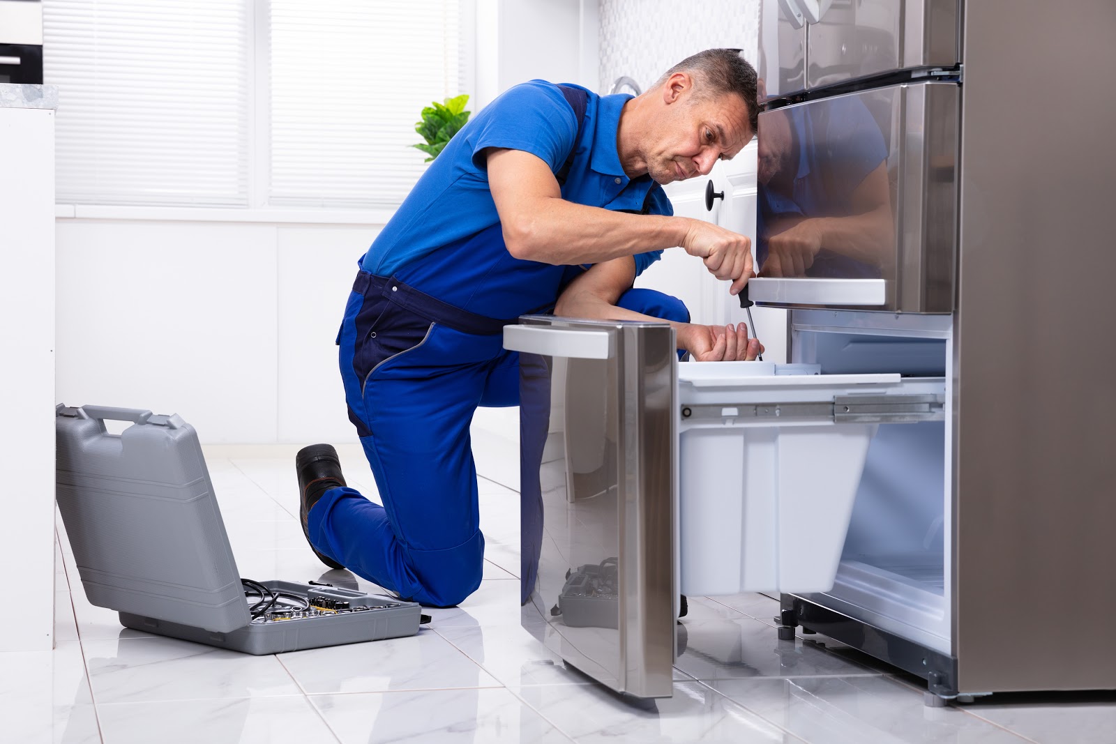 Technician servicing a lower compartment of a residential refrigerator