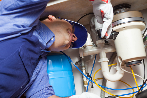 Technician carefully inspecting kitchen appliance connections during an in-home service visit